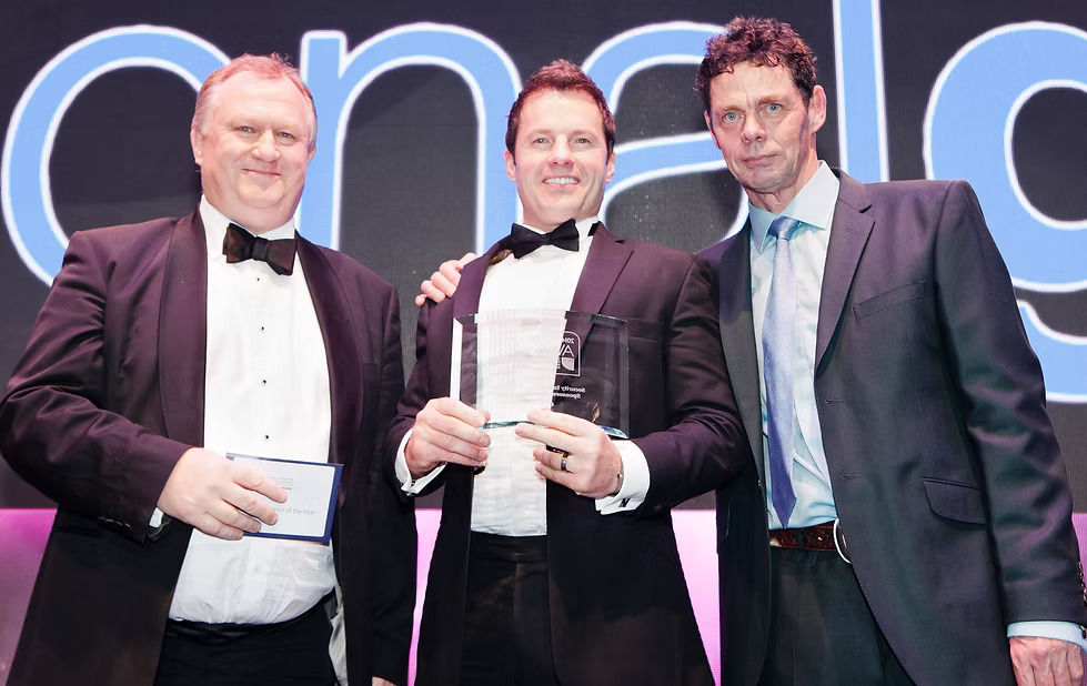 Jason Mace holds award trophy, with comedian and host Rich Hall 