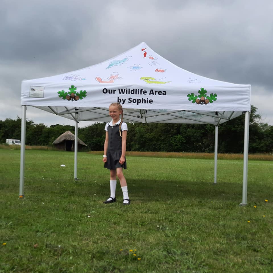 A little girl stands in front of a printed gazebo for her school