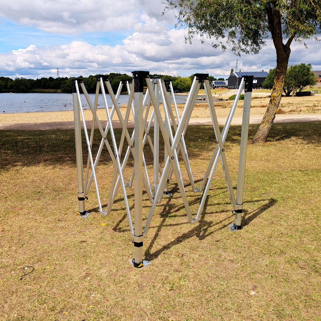 a pop up gazebo frame on grass in front of a lake