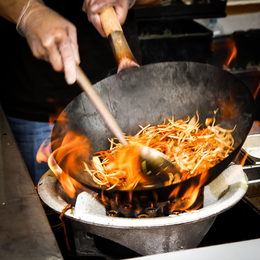 somebody cooks noodles in a large wok